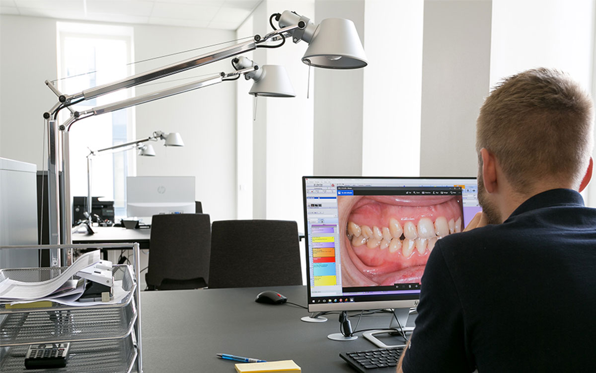 Pracownik kliniki stomatologicznej w Allborgu siedzi przy biurku i przegląda dokumentację medyczną. Z przodu widać otwarty komputer ze zdjęciem pacjenta.